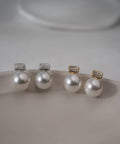 Silver and light gold 10mm shell pearl and baguette cut zirconia drop earrings laid on a soft grey surface