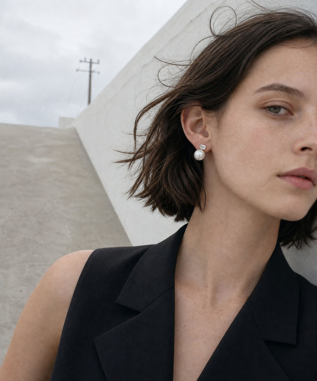 Model outdoors in a black vest wearing the silver 10mm shell pearl and baguette cut zirconia drop earrings