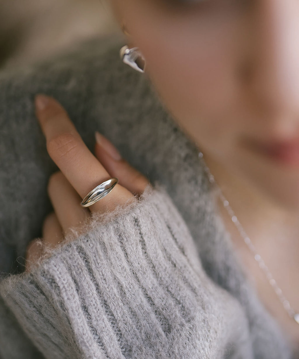 Model in a grey knit wearing the sterling silver ripple wave ring, hand resting at her chest