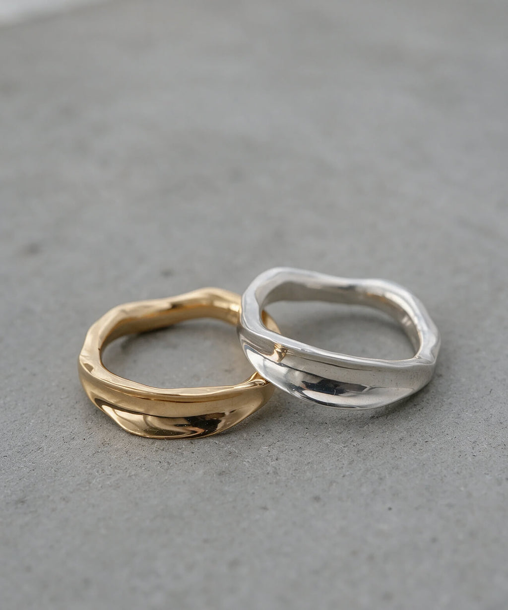 Silver and gold ripple wave rings side by side in soft daylight