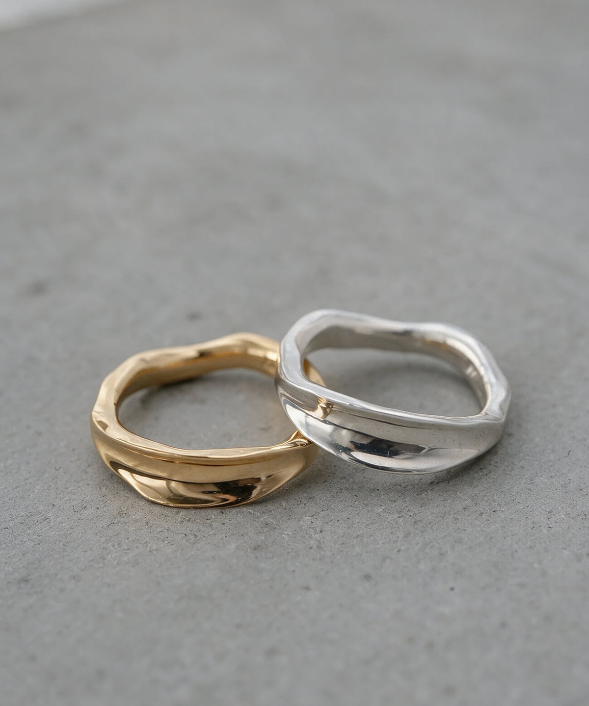 Silver and gold ripple wave rings side by side in soft daylight