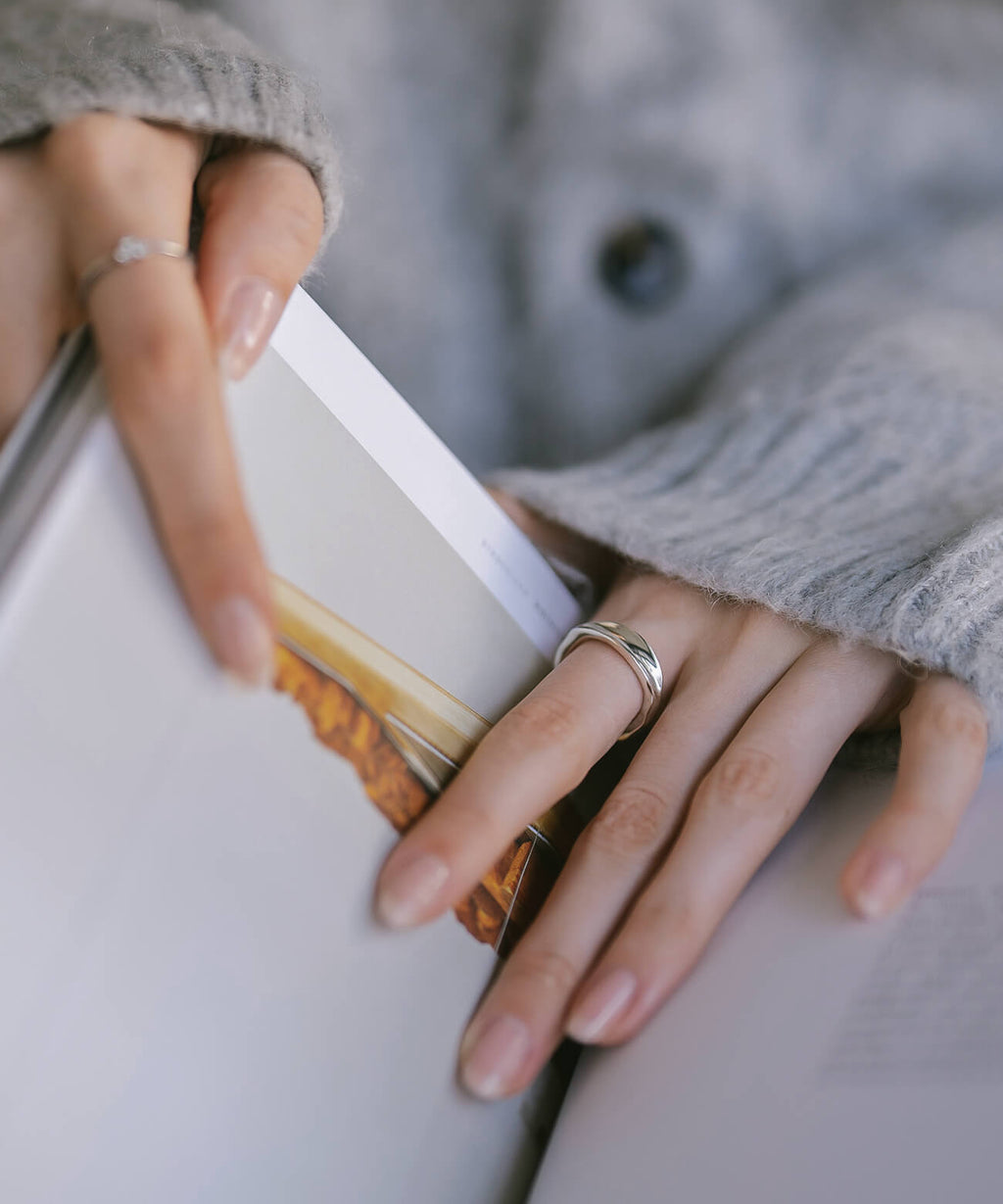 Hand against a grey knit sleeve wearing the sterling silver ripple wave ring