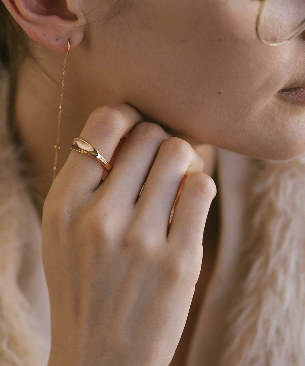 Hand at the shoulder wearing the 18K gold plated ripple wave ring
