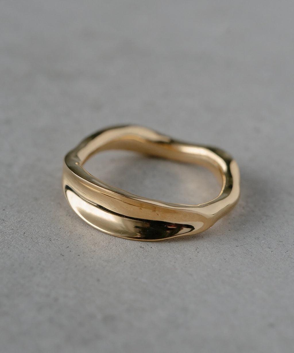 18K gold plated ripple wave ring standing on a concrete surface