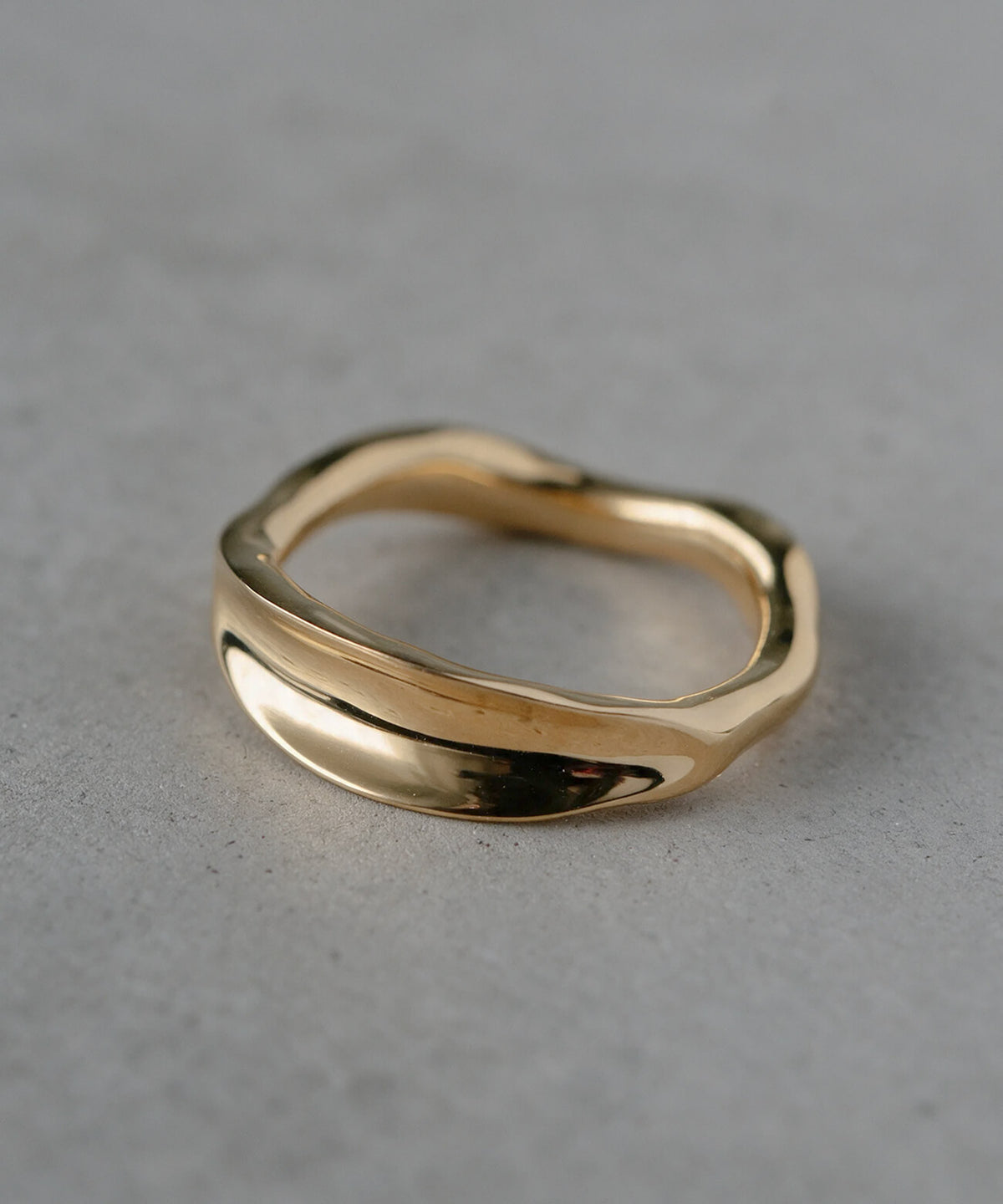18K gold plated ripple wave ring standing on a concrete surface