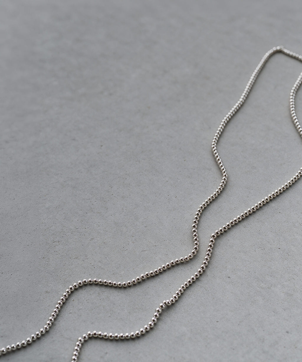 Sterling silver 4mm ball chain long necklace laid in a curve on a grey surface