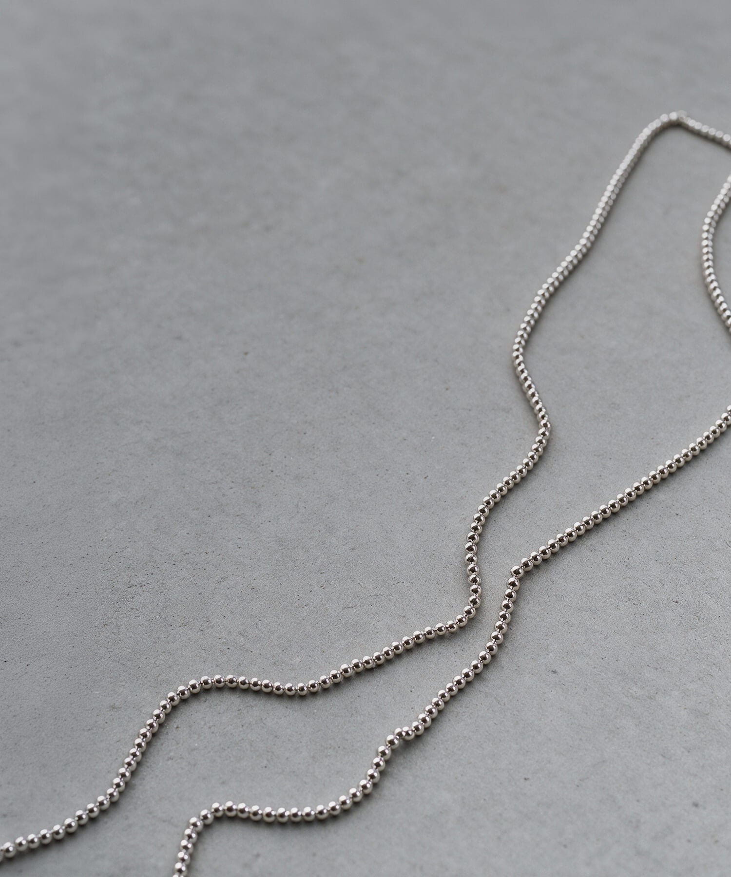 Sterling silver 4mm ball chain long necklace laid in a curve on a grey surface