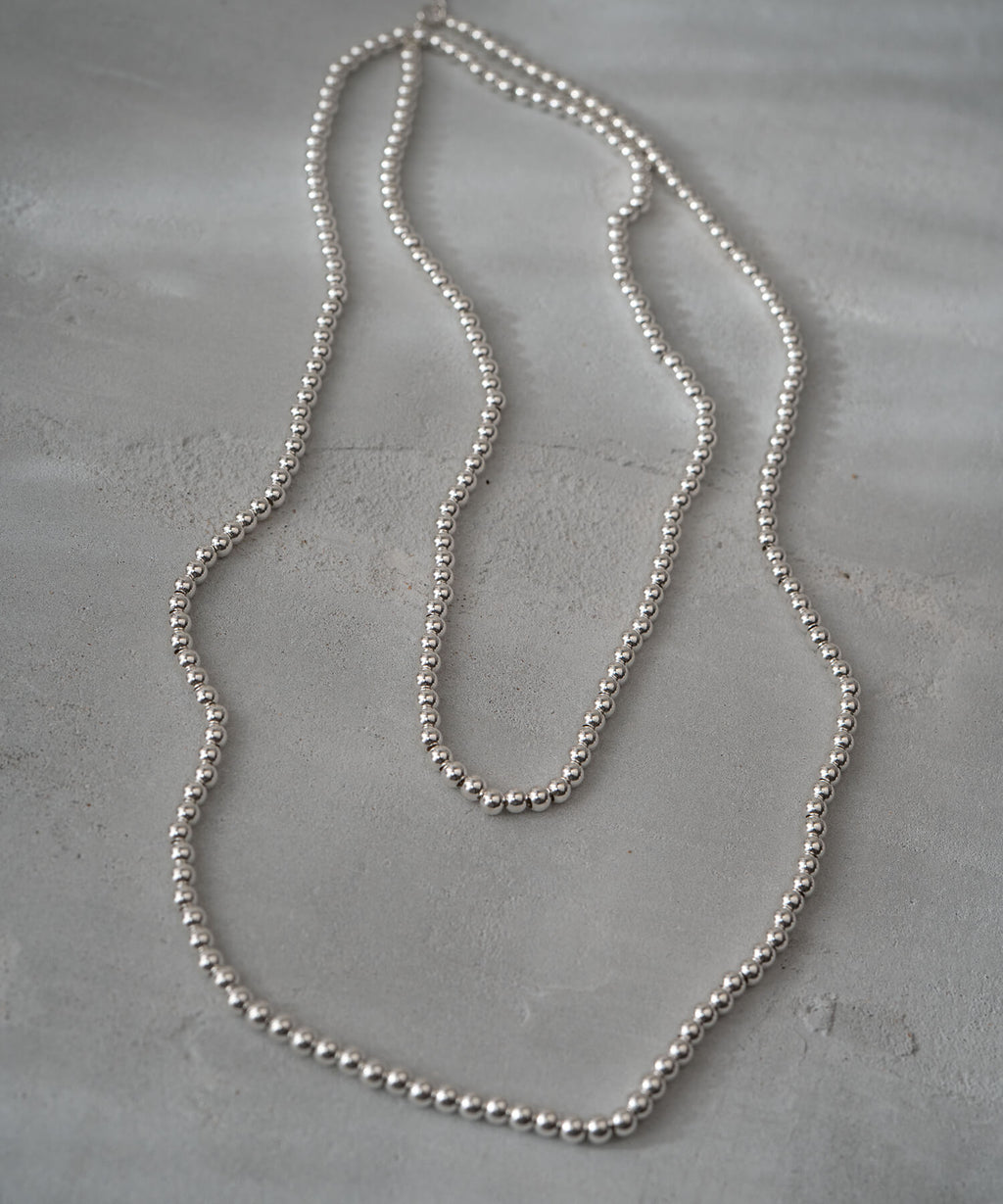 Full length of the silver ball chain necklace laid on a concrete surface