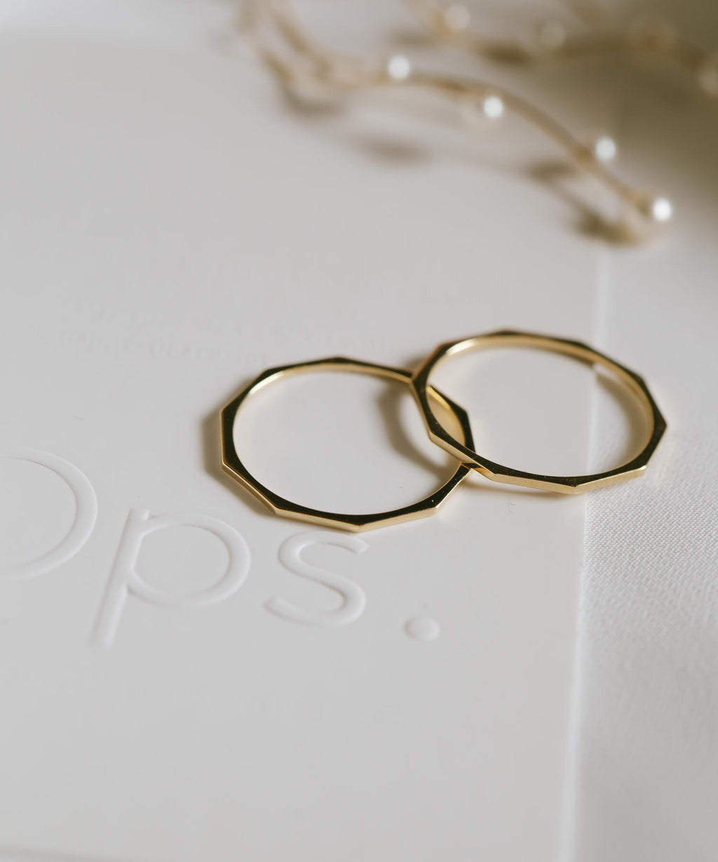 Two 18K gold decagon skinny rings on an embossed card