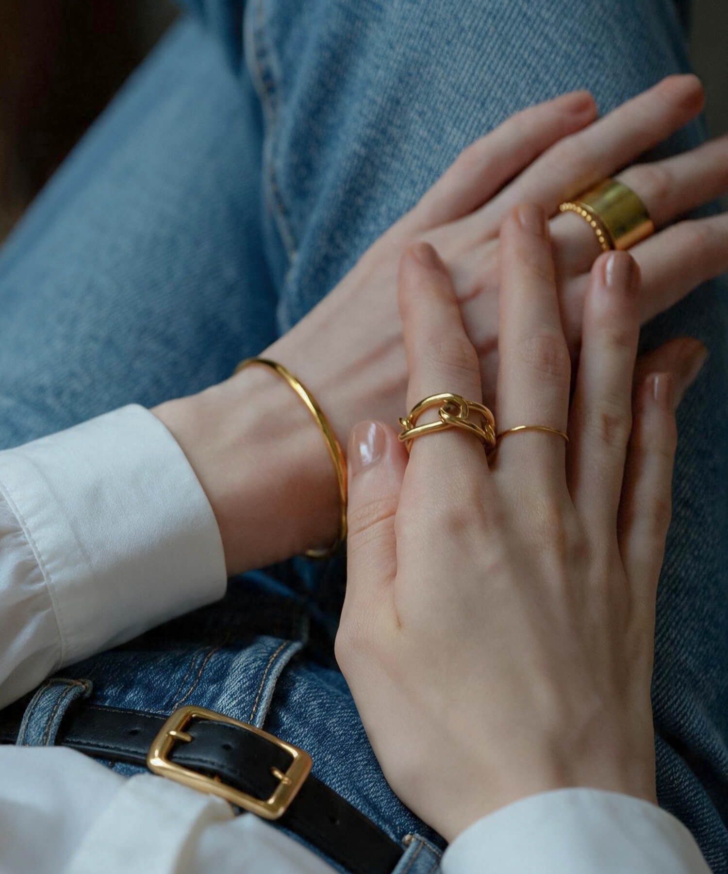 Hands in denim wearing the 18K gold plated chunky chain ring stacked with thin rings